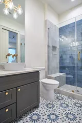 Grey vanity with a vessel sink and gold tap, beside a blue-tiled shower over patterned floor tile
