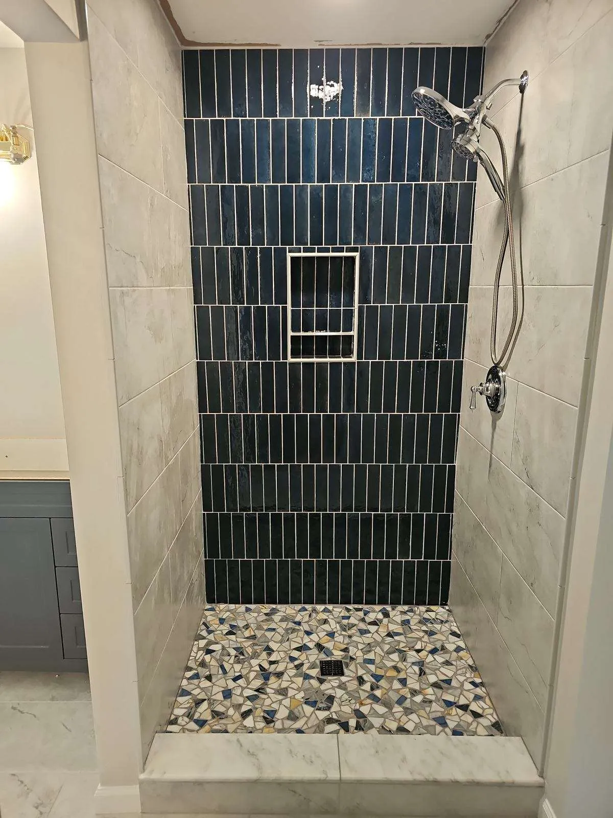Walk-in shower in vertical petrol-blue tile with a pebble pan